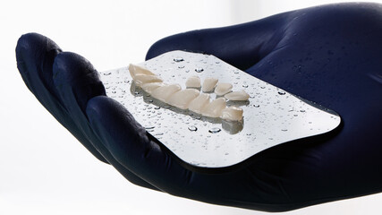 Ceramic dental crowns in the hand of the doctor on the glass