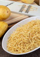 Potato straw or shoestring potato in a white plate with raw potatoes