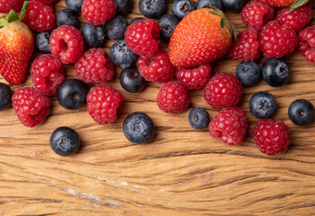 Raspberries, strawberries and blueberries over wooden table with copy space