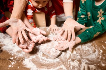 Fototapeta premium Mom and children bake cookies in the kitchen and decorate cookies on Christmas Eve, the top view. Making christmas cookies