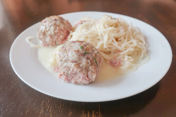 Portion of meat cutlets with spaghetti, sprinkled with sauce on a white plate in a restaurant
