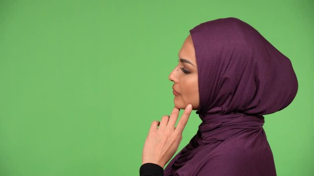 A young beautiful Muslim woman looks to the side and thinks about something - closeup - green screen background