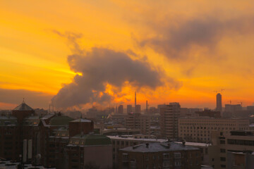 Cityscape with fiery yellow dawn and picturesque smoke from the thermal power plant pipes.