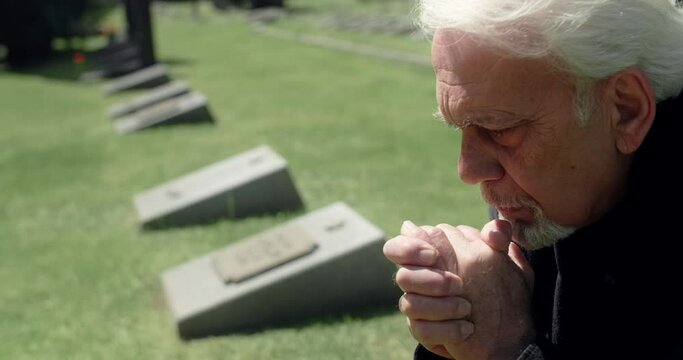 Sad old gray haired man prays on the grave at the cemetery, sorrow and sadness about lost of close people, 4k 60p Prores
