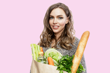 Young woman with a paper bag with groceries. Beautiful smiling blonde. Healthy food, vitamins and veganism. Isolated on a pink background.