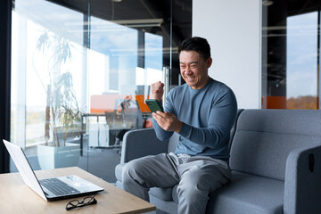 Close-up photo of male businessman using phone in modern office, asian looking at phone display and smiling, online call