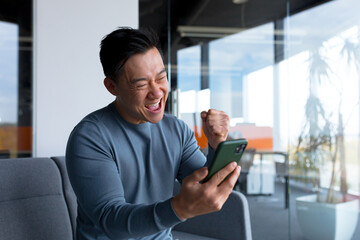 Successful and happy asian businessman man celebrating victory sitting and working in modern office...