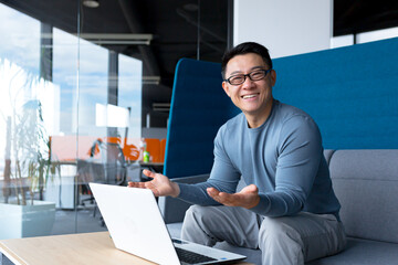 Cheerful teacher looks at the webcam, conducts online classes, Asian man works remotely