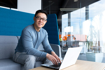 Portrait of male teacher, Asian working from training center office, remotely with laptop, looking at camera and smiling