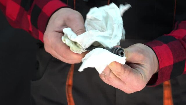 A mechanic in the workshop holds a rag in his hands and cleans a metal part from the car engine. Car washing and maintenance. Dirty hands of an auto mechanic close-up