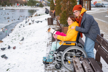 A woman in a wheelchair walks with her friend and a dog by the lake in winter.