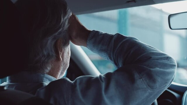 Stressed old businessman feeling headache in car, stop the car, keeping hand to head and feeling anxiety.
