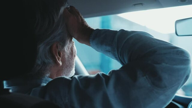 Stressed old businessman feeling headache in car, stop the car, keeping hand to head and feeling anxiety.
