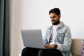 Working from home concept. Indian man using laptop computer. Asian man relaxed and sitting on sofa indoor.
