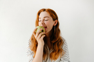 Close up portrait of beautiful young woman biting a green apple, having a snack after studying. Vegetarian food concept