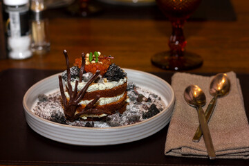 beautiful biscuit cake with cloudberries decorated with chocolate decor on a white dish in a restaurant close-up