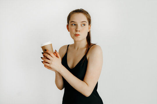 Young woman with a ponytail, in a black dress, holding a with a cup of coffee