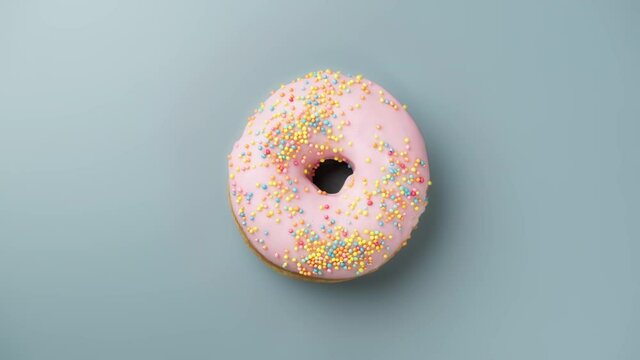 Tasty pink donut with sprinkles rotating at light blue or gray background. Bakery and food concept. Sweet dessert. 4K, UHD