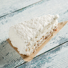 A piece of cake with white coconut chips on a wooden background made of old boards.