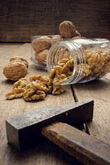 Fototapeta na wymiar Nuts coming out of a glass jar and hammer on a wooden table in a dark environment.. High quality photo