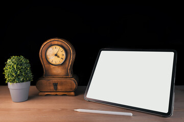 Tablet and pen with clock and plant on black background