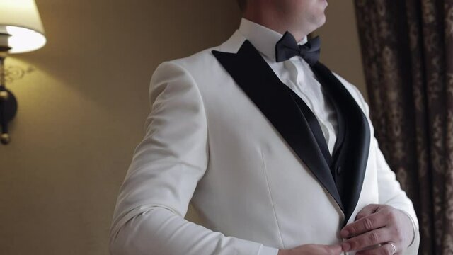 Groom buttoning white jacket with hands. Stylish man in suit fastens buttons and straightens his jacket preparing to go out. Businessman getting ready before date or meeting fashion style weight fit