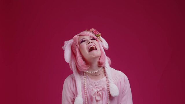 Pink sad cute candy girl with plush rabbit ears is crying, handsome guy makes unexpected surprise given a lollipop and make her happy on red background. Baby stop crying solution concept. Couple mimes