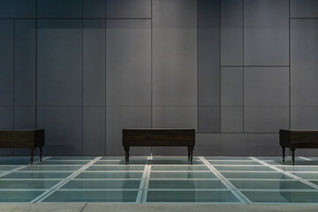 Glassy floor with three old dressers standing on it in front of gray tiles on wall