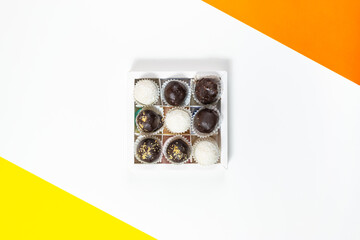 Square white box with round chocolate candies on a white background with yellow and orange accents.