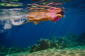 Fototapeta na wymiar a girl in a pink swimsuit in a mask and fins swims underwater