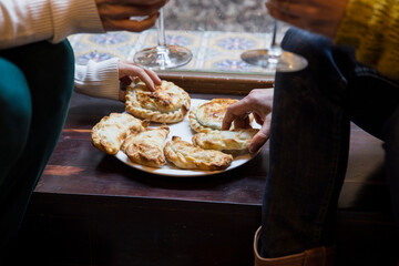 Close up of lesbian couple hands making a toast for Valentine day while hold a latin empanada food and a glasses of wine.