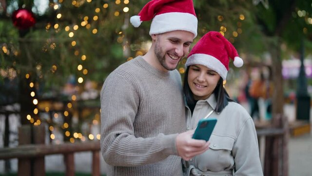 Young couple wearing christmas hat make selfie by the smartphone at park