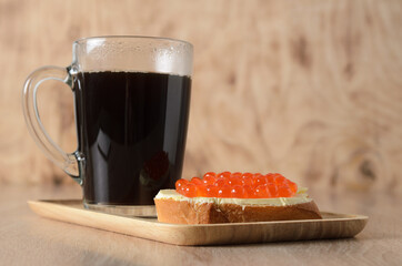 A sandwich with butter and red caviar with a mug of hot black co