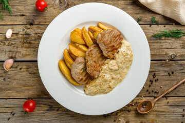 Pork medallions with fries and creamy sauce on white plate top view on wooden table