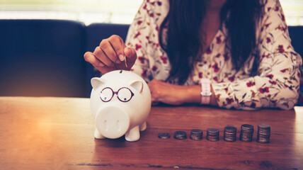 Women hand holds a coin in a piggy bank for future home purchases. Save money. Economic concept