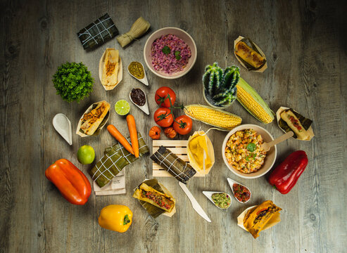 I LOVE FOOD SERIES. Latin American food on a wooden table with fresh, healthy and natural ingredients, such as corn, red pepper, hallacas, humita, tamale, carrot, tomato, lime, perfect for a dinner.