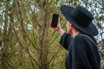Young woman with a hat concerned looking for signal with his smartphone in the woods. Lost hiker with no gps. Girl looking for internet service on a forest. Comunnication.
