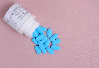 Scattering blue pills from bottle on pink background top view.