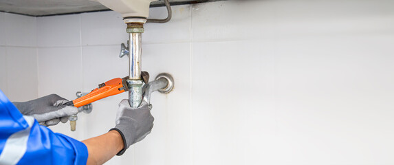 Fototapeta Technician plumber using a wrench to repair a water pipe under the sink. Concept of maintenance, fix water plumbing leaks, replace the kitchen sink drain, cleaning clogged pipes is dirty or rusty. obraz