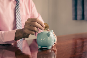 The hand of a businessman puts coins in a piggy bank, saves money with coins, steps into a...