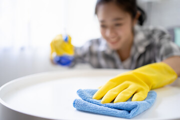 Asian woman in protective gloves and is wiping dust using spray while cleaning her house.
