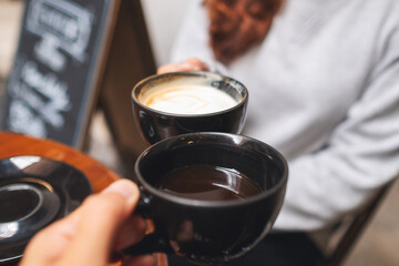 Closeup image of a couple people clinking coffee cups together in cafe