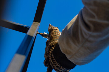 The man tightens the nut with a wrench. A young, gloved factory worker uses a wrench to tighten a nut on a stainless steel pipe joint. Installation of equipment.