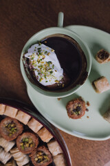 close up drinking chocolate in matching green cup and plate with assorted baklava desserts on wood table