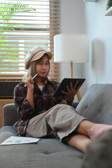 Asian woman sitting on sofa and working with digital tablet.