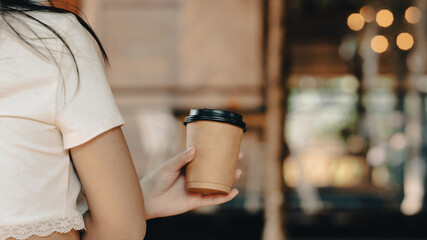 Young woman holding disposable paper cup of coffee while sitting in modern coffee shop.