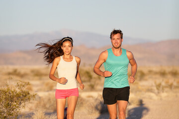 Runners couple running long distance ultra trail run race. Runner man and sport woman training cardio outside in cross country sunset landscape. Fit male Caucasian fitness model, Asian female athlete.