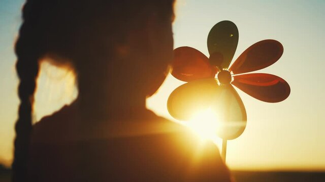 kid pinwheel. little baby girl silhouette play with windmill toy wind in the park. happy family kid dream concept. baby girl play toy pinwheel the glare of the sun at sunset in fun the park