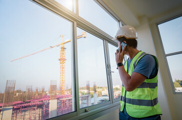 Engineer manager construction management standing in office building in construction process next to window use smart phone inspector construction site check drawing and business workflow of building