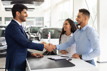 Smiling middle-eastern man and woman buying car at salon